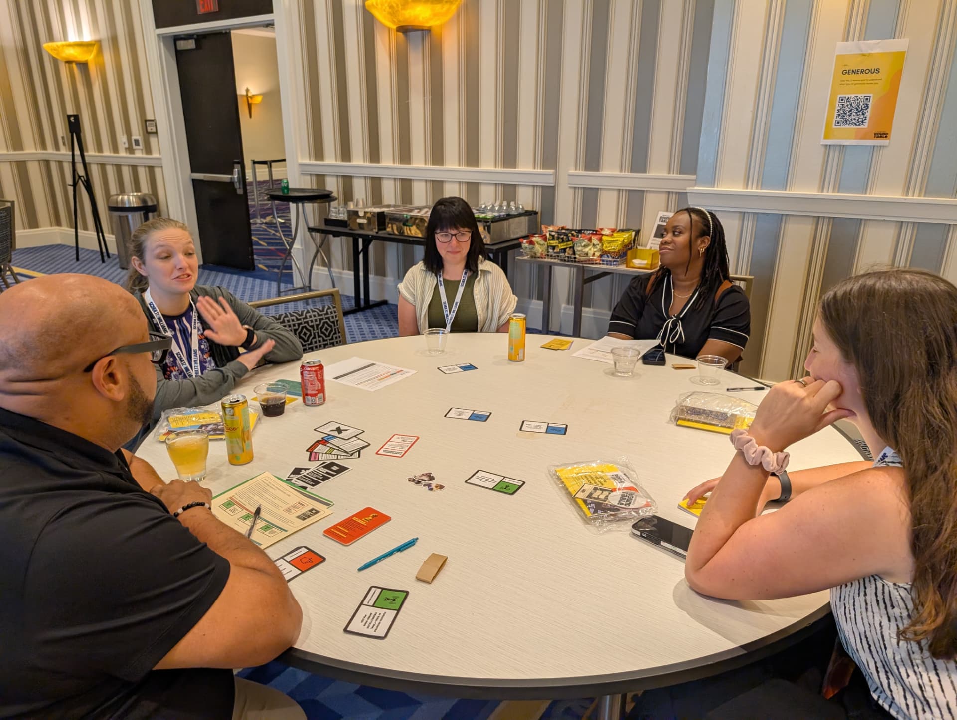 Five players in conversation over a spread of Generosity Roundtable cards.