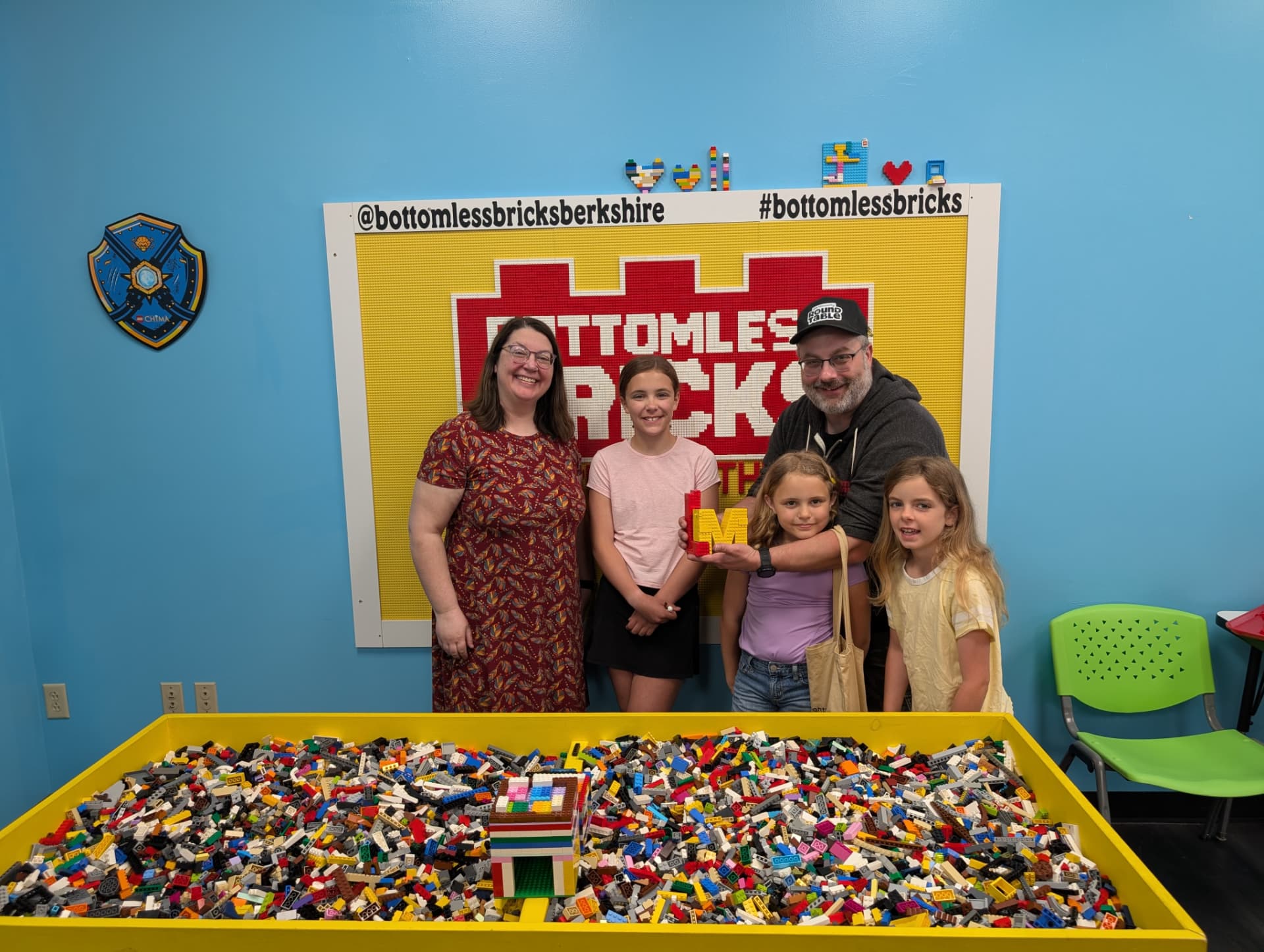 A family of five poses with a Roundtable brick build in a LEGO play space.