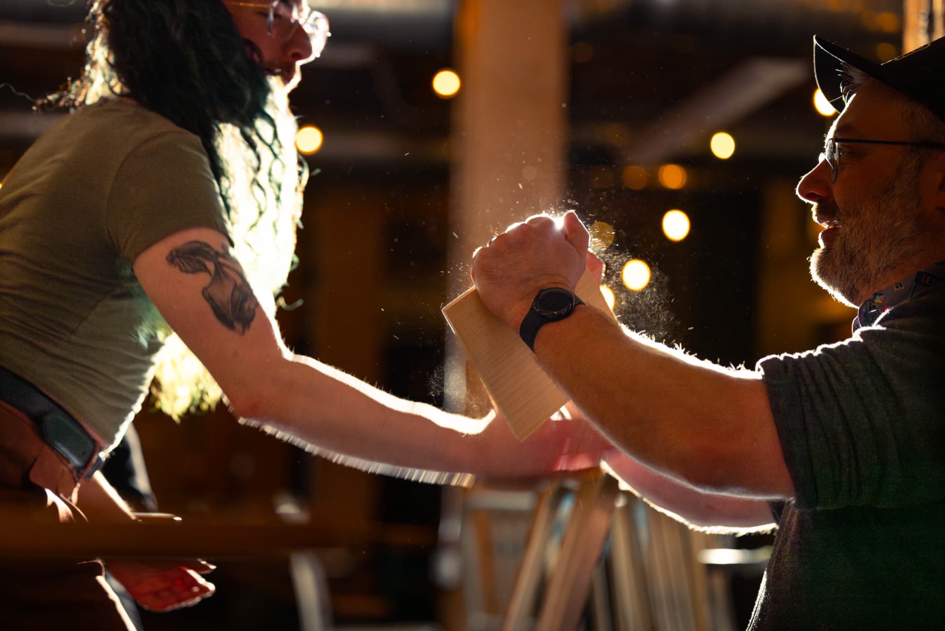 Two people clasp hands over a wooden card in warm backlight at the end of a session.